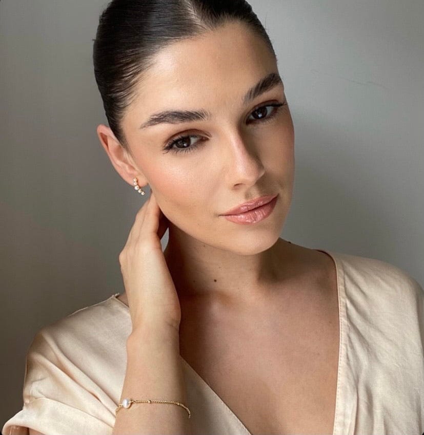 A woman with slicked-back hair and jewelry poses in front of a gray background, wearing Bridal Pearl Bar Stud.