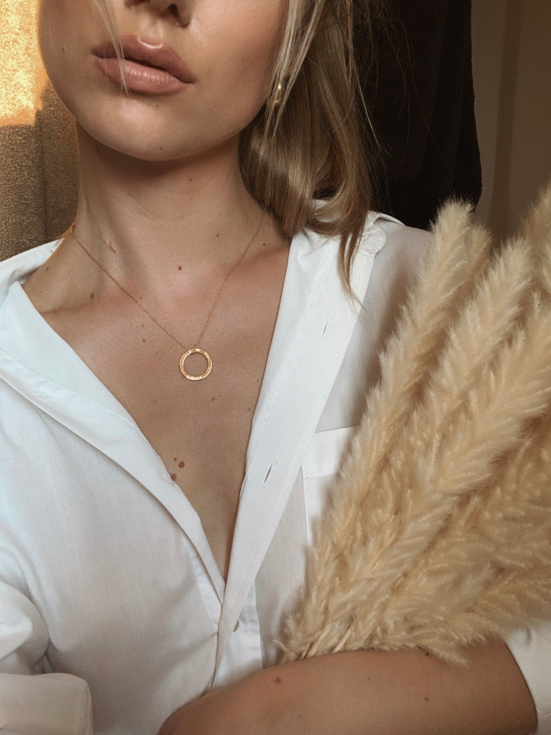 Woman in white shirt wearing a gold necklace, holding pampas grass and the Ní neart go cur le chéile.