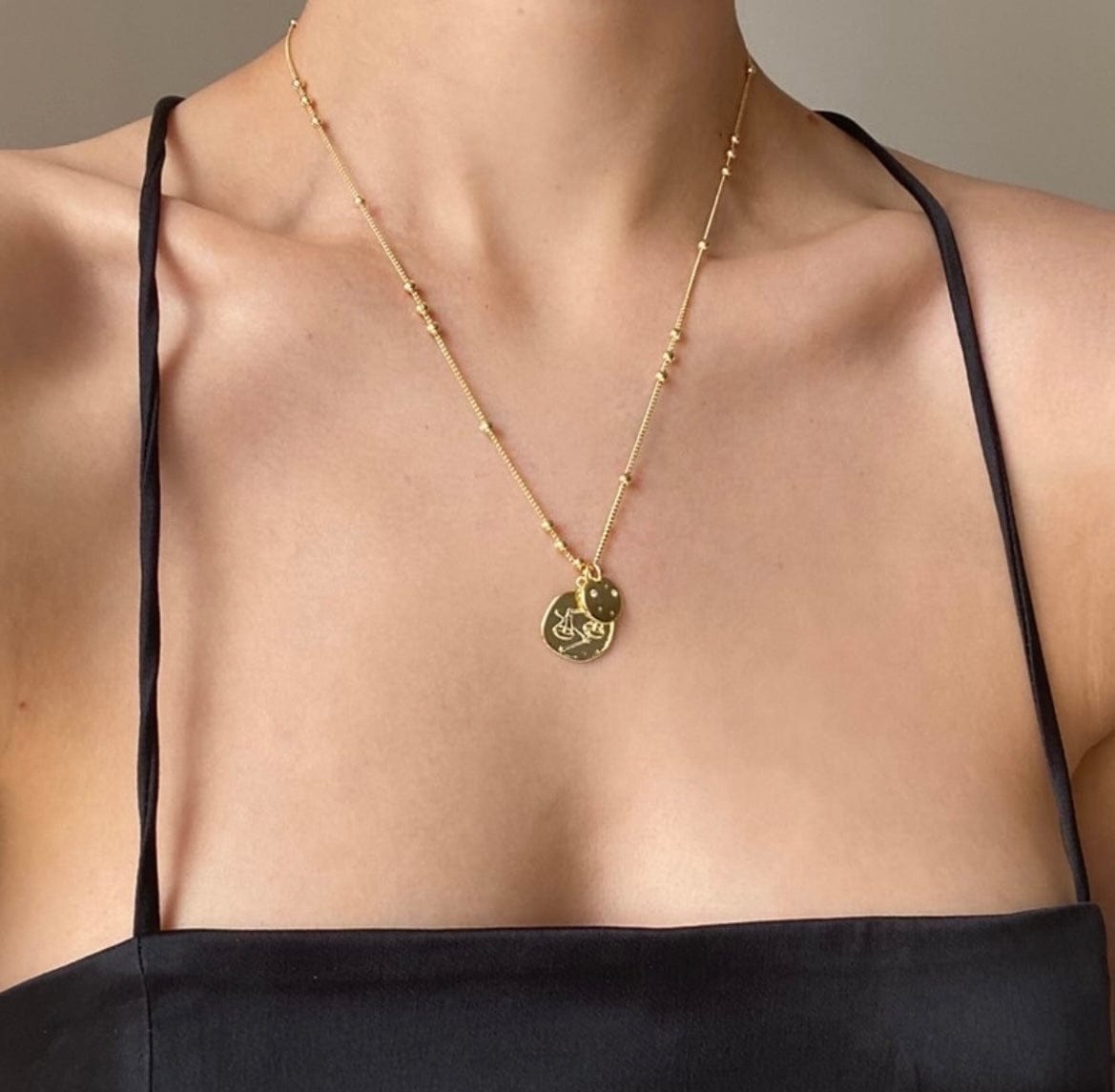 Close-up of a person wearing a gold beaded Sagittarius Zodiac Coin necklace with two coin pendants.