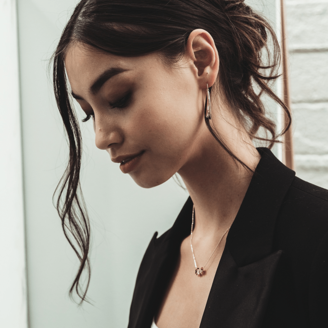 A woman with dark hair in a black blazer looks down while wearing earrings and a Trio Star Charm Necklace.