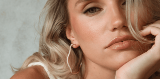 Close-up of two shiny gold hoop earrings on a white fabric surface.