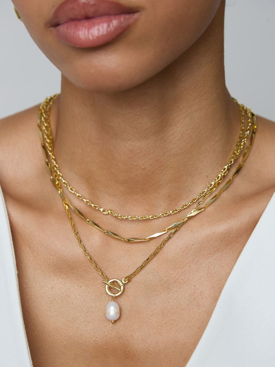 A close-up of a model wearing a layered gold necklace set with a teardrop pearl pendant.