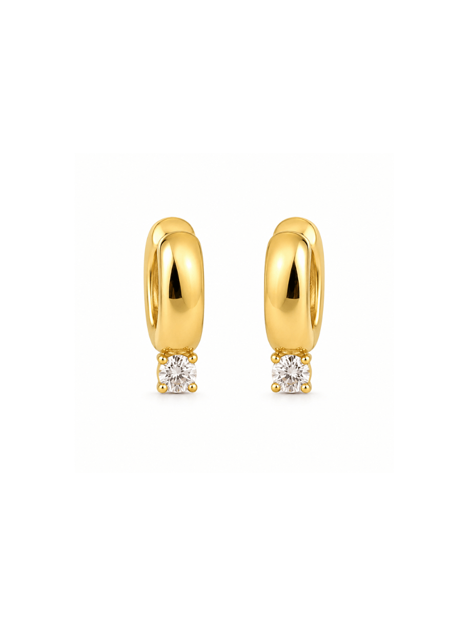 A pair of gold huggie hoop earrings, each featuring a small round clear gemstone in a prong setting at the bottom, displayed on a clean white background.