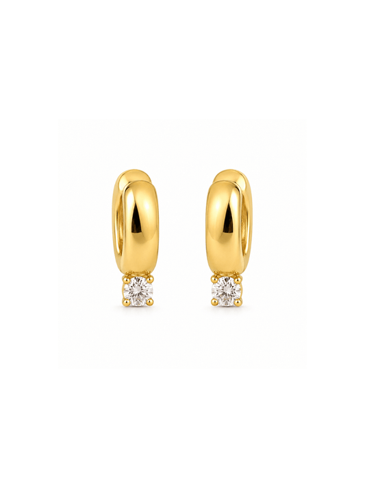 A pair of gold huggie hoop earrings, each featuring a small round clear gemstone in a prong setting at the bottom, displayed on a clean white background.