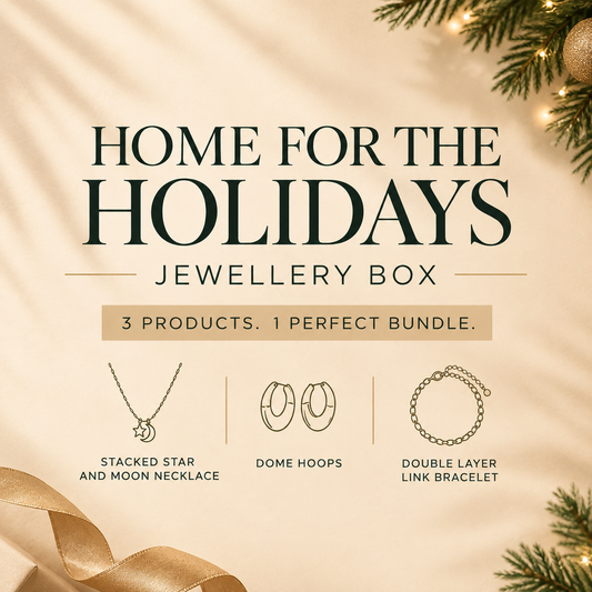 'Home for the Holidays Jewellery Box' featuring three jewelry items: a stacked star and moon necklace, dome hoops, and a double layer link bracelet, set against a warm beige background with holiday pine branches and a gold ribbon.