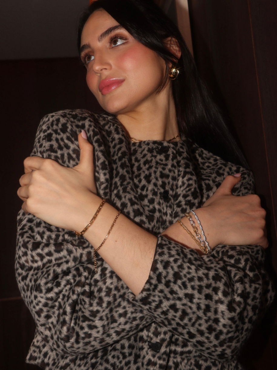 A woman in a patterned jacket with gold jewelry, arms crossed, wearing a Mixed Metal paperclip Bracelet.