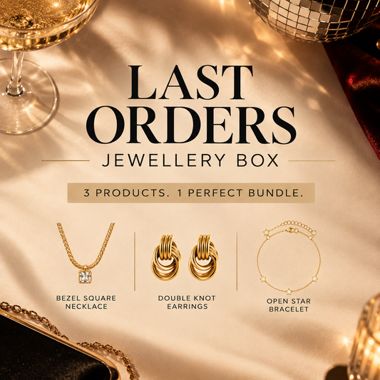 'Last Orders Jewellery Box' featuring three gold-toned jewelry items: a bezel square necklace, double knot earrings, and an open star bracelet, displayed on a draped champagne-colored fabric with elegant props.