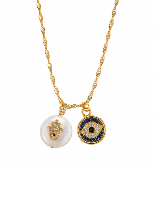 A gold chain necklace featuring two circular evil eye and hamsa hand pendants, one with a white pearl-like background and the other with a blue and gold design, set against a plain white background.