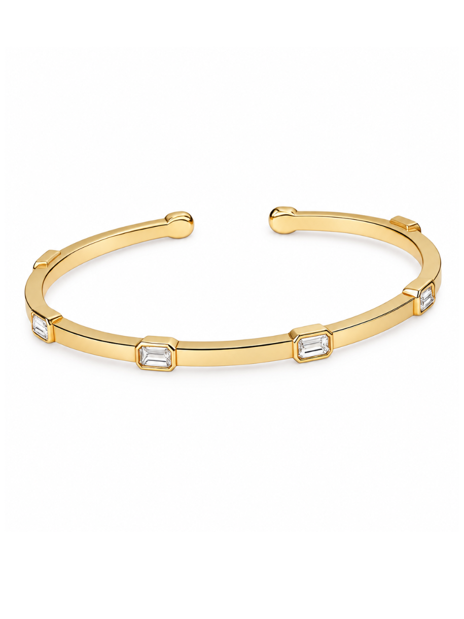A gold-toned open cuff bangle bracelet featuring five rectangular clear baguette-cut stones spaced along the front, set against a plain white background.
