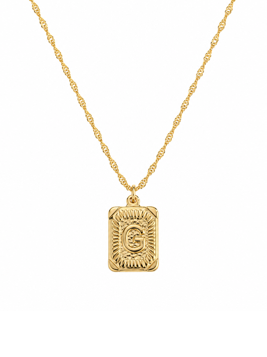 A gold necklace featuring a rectangular pendant with a textured sunburst pattern and an engraved initial letter in the center, suspended from a twisted chain against a plain white background.