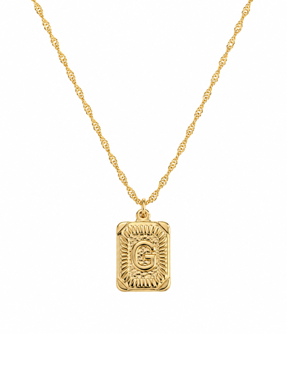 A gold necklace featuring a rectangular pendant with a textured sunburst pattern and an engraved initial letter in the center, suspended from a twisted chain against a plain white background.