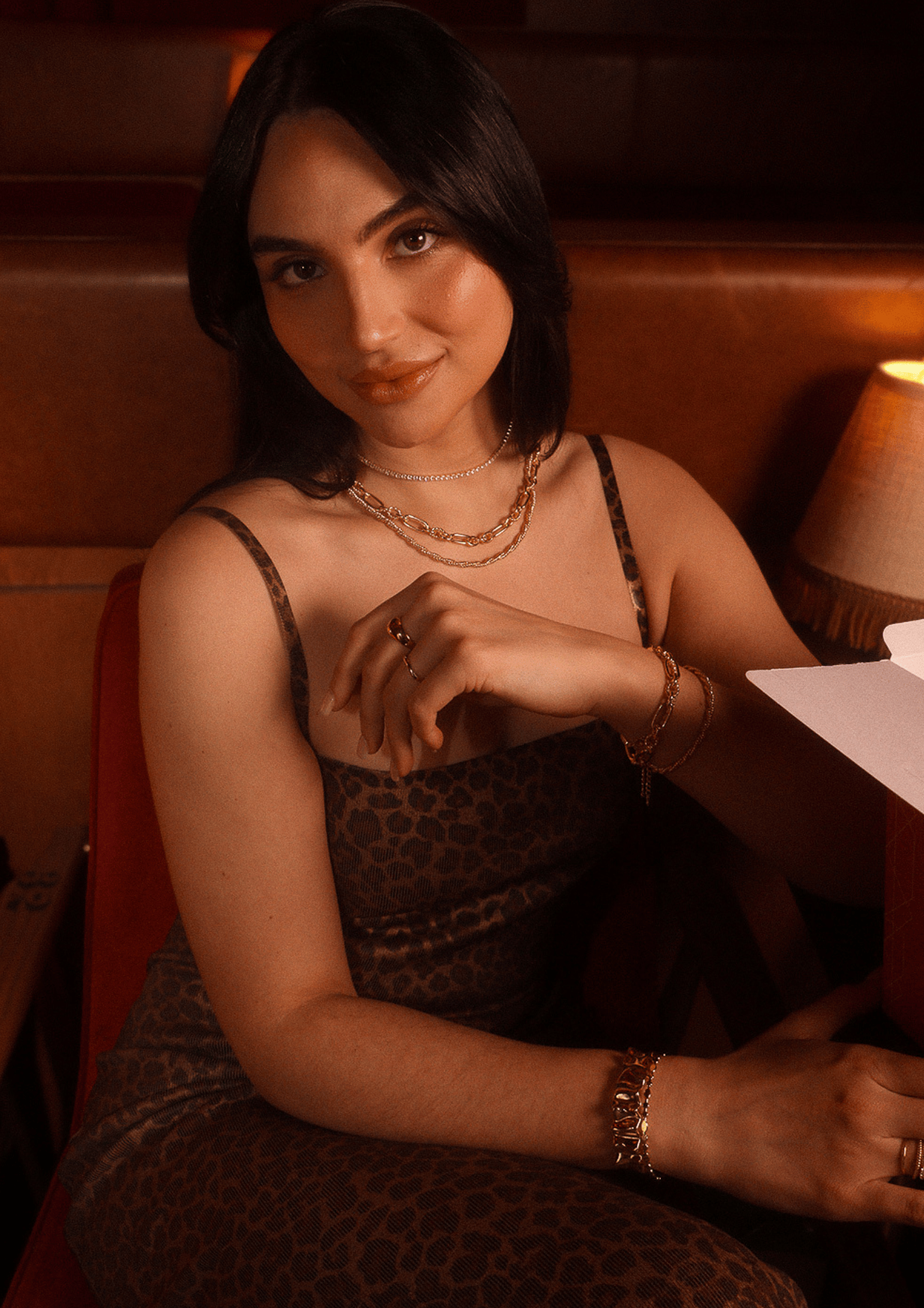 Woman in a leopard print dress and gold jewelry, including a Savoy Link Necklace, sitting in a booth.