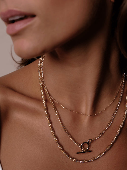 Close-up of a person's lower face and neck, wearing three layered gold necklaces of different styles.